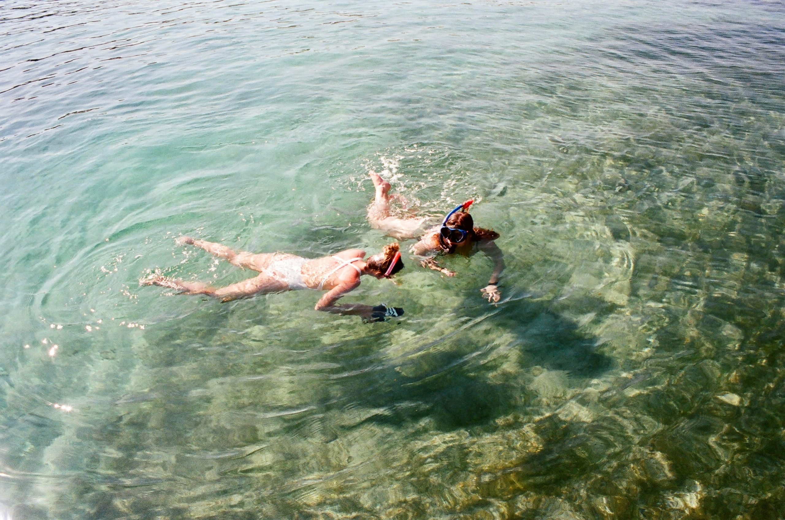 two women in clear blue green water with snorkels on enjoying the view of the ocean floor